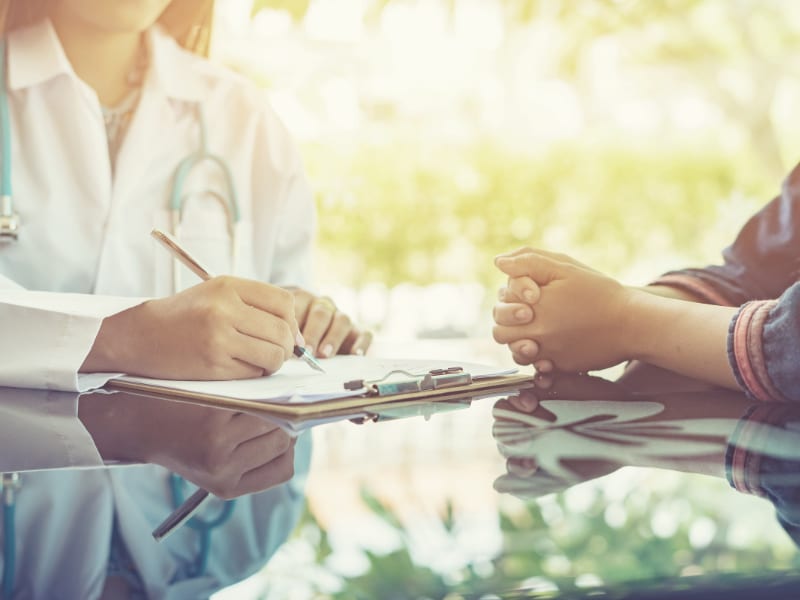 Ärztin und Patient sitzen an einem glänzenden Tisch, Ärztin macht Notizen