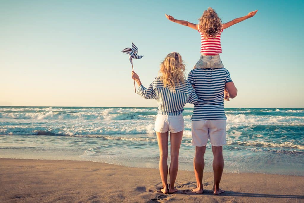 Pärchen am Strand, auf den Schultern des Mannes sitzt ein kleines Mädchen