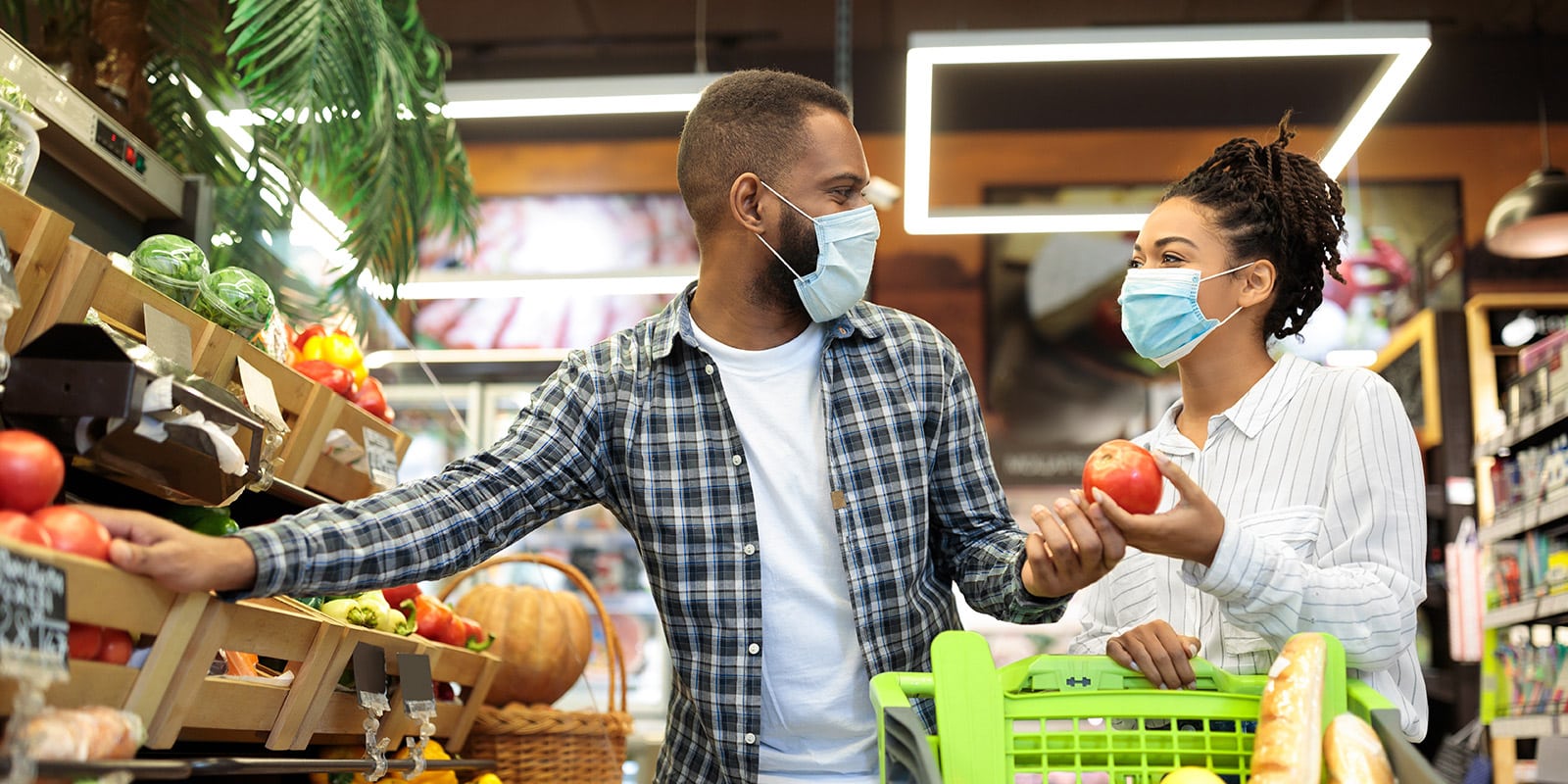 Ein junge Paar mit medizinischen Masken kauft im Supermarkt Obst ein