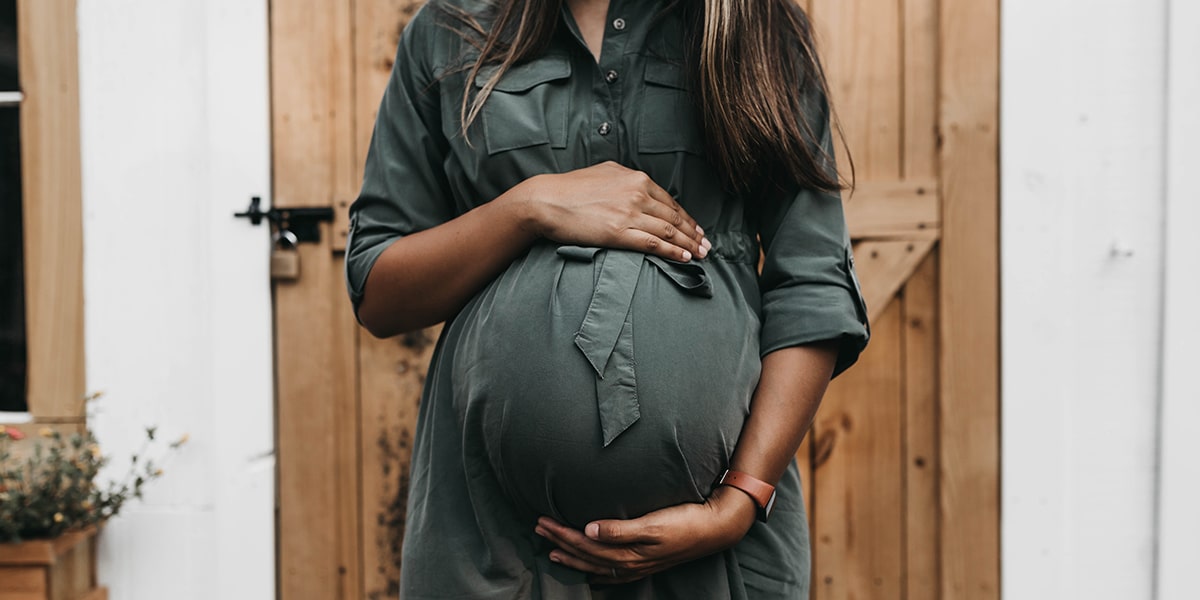 Schwangere Frau mit dunkelgrünem Kleid hält ihren Bauch