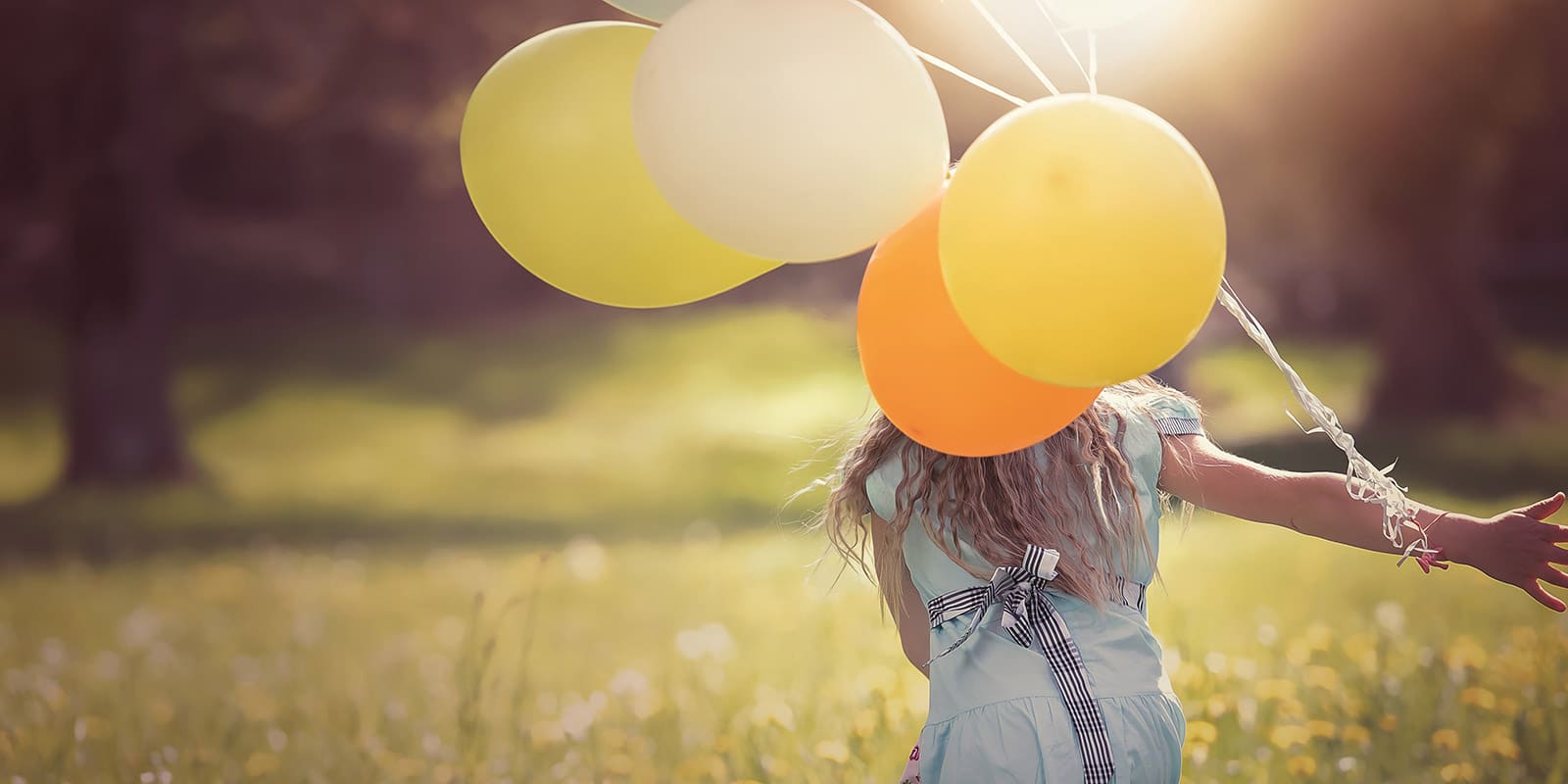 Kleines Mädchen läuft auf Blumenwiese und hat Luftballons an ihren Arm geknotet