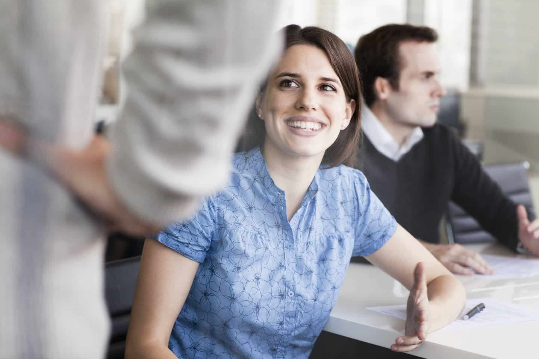 Lächelnde junge Frau mit Business-Bluse im Gespräch mit einem Kollegen